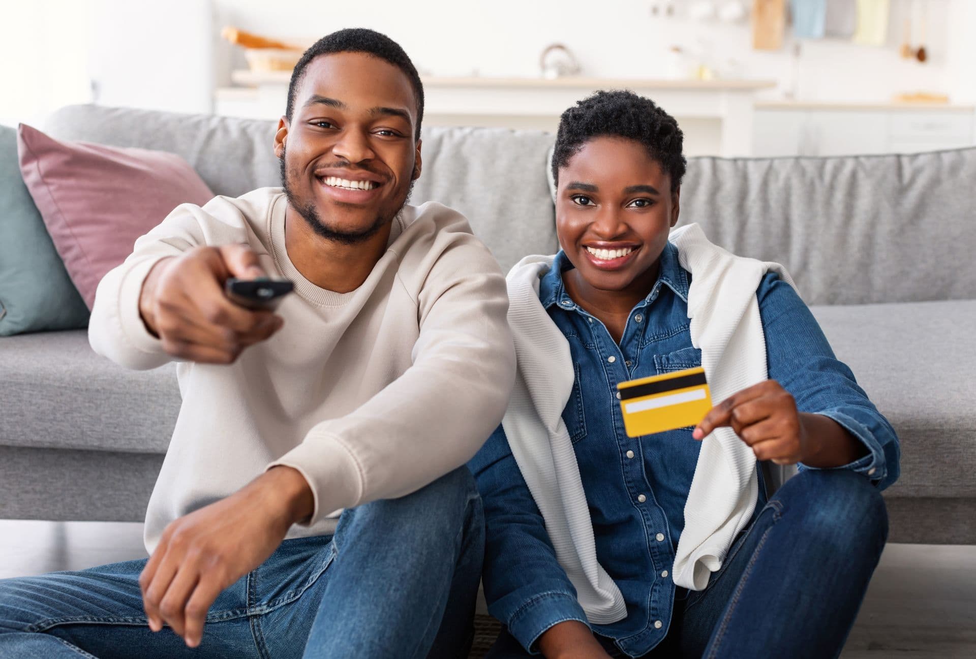 A black couple hold up a credit card as they change channels